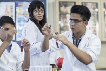 Schüler im Chemieunterricht, die Flüssigkeit in ein Reagenzglas pipettieren, beobachtet von einem Lehrer - ZEF006148