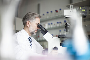 Scientist in laboratory looking through microscope - RBF002526