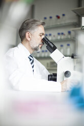 Scientist in laboratory looking through microscope - RBF002528