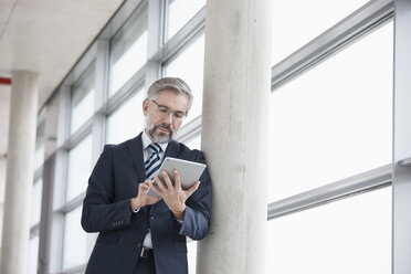 Businessman leaning against column using digital tablet - RBF002551