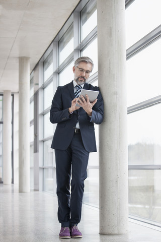 Geschäftsmann lehnt an einer Säule und benutzt ein digitales Tablet, lizenzfreies Stockfoto