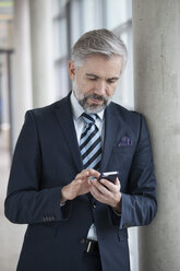 Businessman leaning against column using smartphone - RBF002560