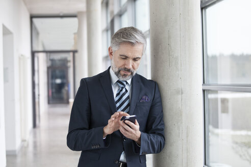 Geschäftsmann lehnt an einer Säule und benutzt ein Smartphone - RBF002561