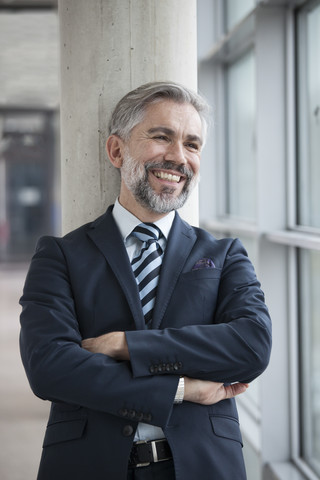 Glücklicher Geschäftsmann lehnt an einer Säule, lizenzfreies Stockfoto