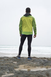 Spain, Valdovino, rear view of jogger standing at the ocean - RAEF000085