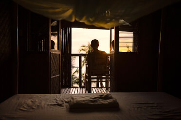 Philippinen, Apo Island, Mann auf der Terrasse einer Holzhütte bei Sonnenuntergang - GEMF000128