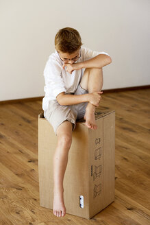 Unglücklicher Junge sitzt auf einem Karton in einem leeren Raum - LBF001086