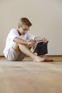 Junge sitzt auf Holzboden und benutzt ein digitales Tablet - LBF001083