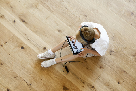 Boy sitting on wooden floor using digital tablet stock photo