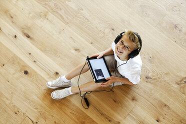 Smiling boy sitting on wooden floor with digital tablet - LBF001082