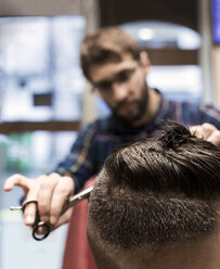 Friseur schneidet einem jungen Mann die Haare in einem Friseursalon - MGOF000164