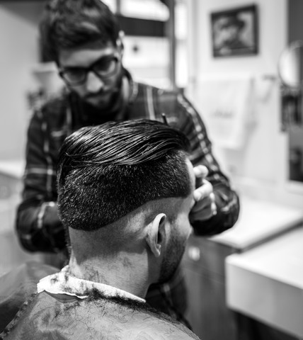 Friseur schneidet einem jungen Mann die Haare in einem Friseursalon, lizenzfreies Stockfoto