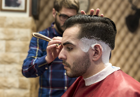 Friseur rasiert die Haare eines jungen Mannes in einem Friseursalon, lizenzfreies Stockfoto