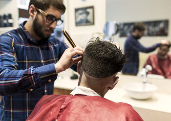 Friseur rasiert die Haare eines jungen Mannes in einem Friseursalon - MGOF000147