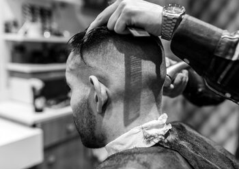 Friseur rasiert den Kopf eines jungen Mannes in einem Friseursalon - MGOF000153