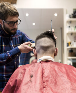 Friseur rasiert die Haare eines jungen Mannes in einem Friseursalon - MGOF000155