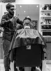 Friseur rasiert die Haare eines jungen Mannes in einem Friseursalon - MGOF000161