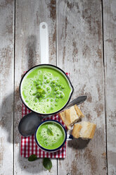 Kochtopf und Becher mit Erbsensuppe, Löffel, Baguettescheiben und Tuch auf Holz - CSF024971