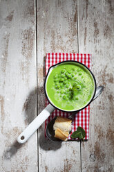 Saucepan of pea soup and sliced baguette on cloth and wood - CSF024975