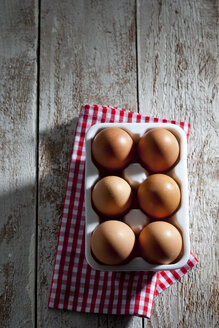Eierkarton mit sechs braunen Hühnereiern Küchentuch und Holz - CSF025012