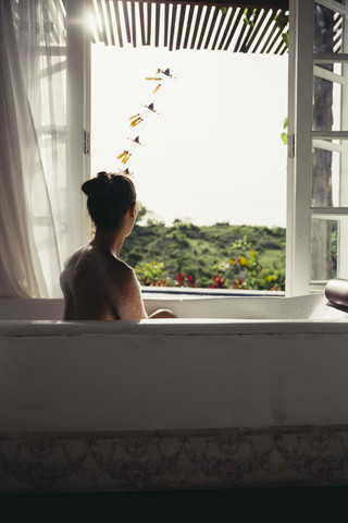 Frau entspannt sich in der Badewanne und schaut aus dem offenen Fenster, lizenzfreies Stockfoto