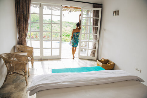 Indonesien, Bali, Frau steht vor geöffneter Terrassentür einer Ferienvilla - MBEF001343