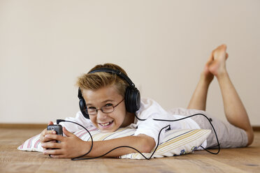 Smiling boy with MP3 Player and headphones lying on wooden floor - LBF001091