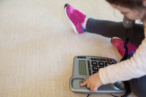 Kleines Mädchen spielt mit dem Telefon und sitzt auf dem Teppich, lizenzfreies Stockfoto