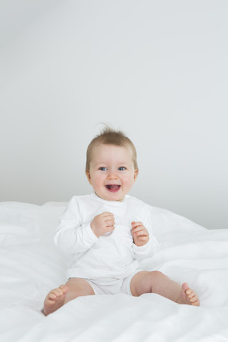 Smiling baby girl sitting on bed stock photo