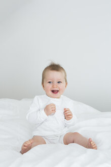 Smiling baby girl sitting on bed - JTLF000088