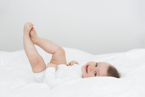 Smiling baby girl lying on bed - JTLF000091