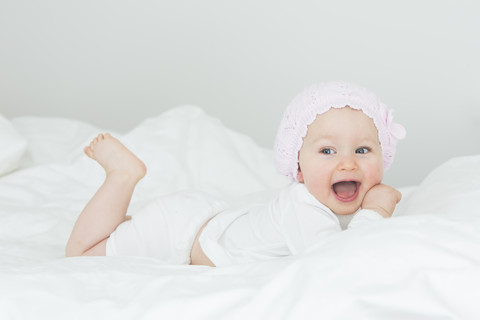 Laughing baby girl with cap lying on bed stock photo