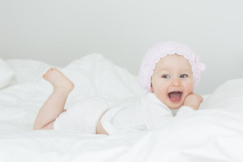 Lachendes kleines Mädchen mit Mütze auf dem Bett liegend - JTLF000099