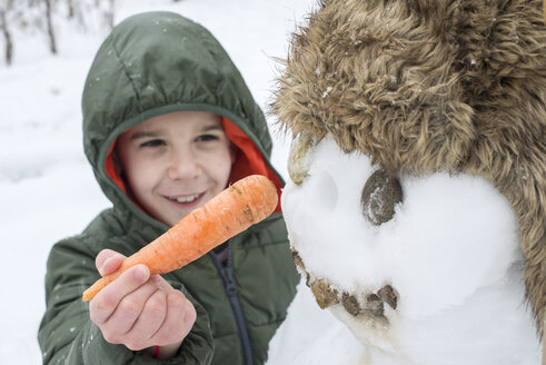 Junge befestigt Karotte an Schneemann - DEGF000392