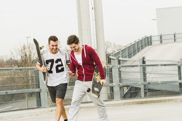 Zwei Freunde gehen mit Skateboard und Mobiltelefon spazieren - UUF003666