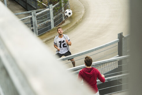 Zwei junge Männer köpfen einen Fußball über den Zaun - UUF003672