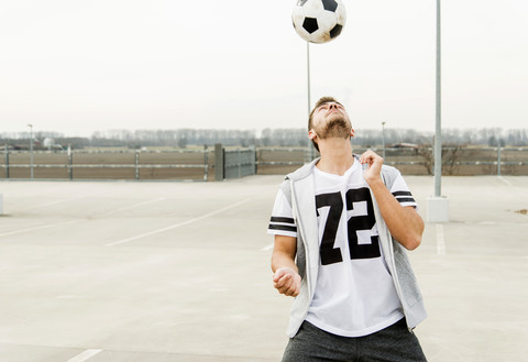 Junger Mann köpft Fußball auf dem Parkdeck, lizenzfreies Stockfoto