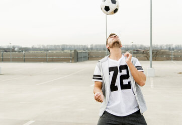 Young man heading soccer ball on parking level - UUF003673