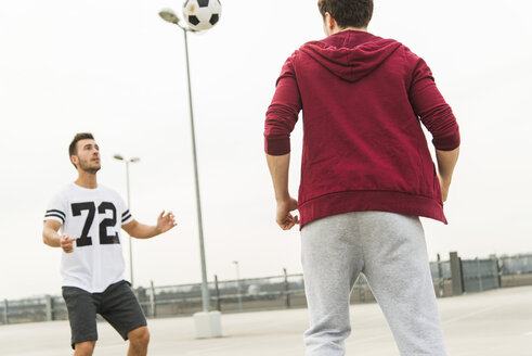 Zwei junge Männer spielen Fußball auf dem Parkdeck - UUF003678