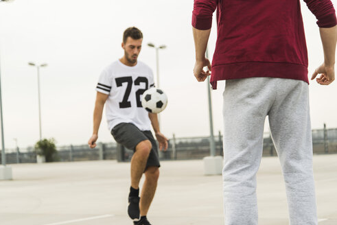 Zwei junge Männer spielen Fußball auf dem Parkdeck - UUF003679