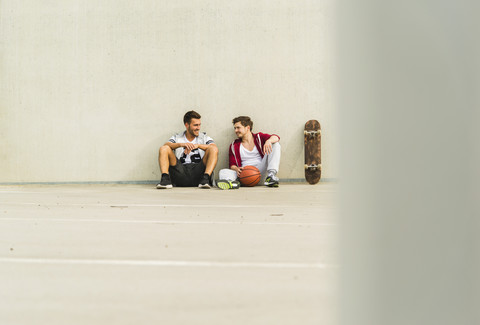 Zwei junge Männer sitzen mit Skateboard und Basketball auf dem Parkdeck, lizenzfreies Stockfoto