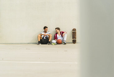 Two young men sitting with skateboard and basketball on parking level - UUF003684