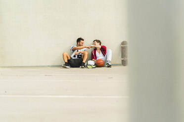 Zwei junge Männer sitzen mit Skateboard und Basketball auf dem Parkdeck - UUF003685