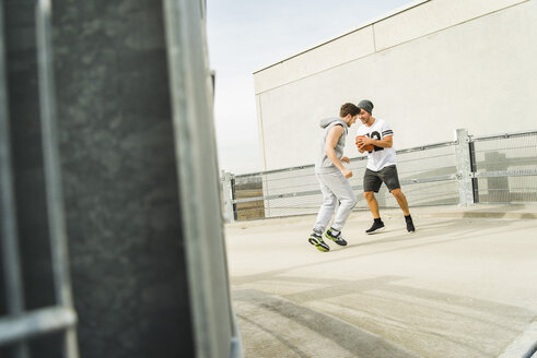 Zwei junge Männer spielen mit einem Fußball auf dem Parkdeck - UUF003694