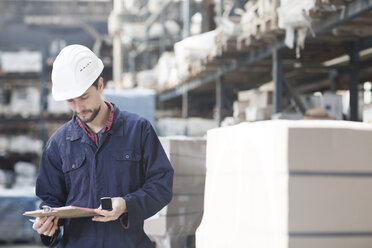 Warehouseman in storehouse holding clipboard - SGF001414