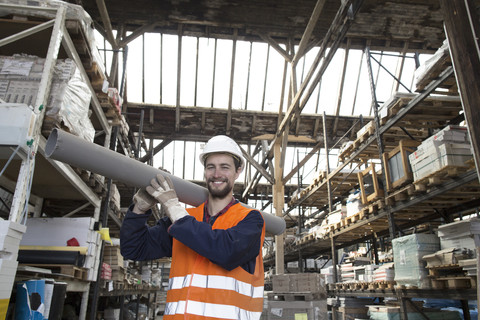 Lächelnder Lagerist im Lagerhaus, der ein Rohr trägt, lizenzfreies Stockfoto