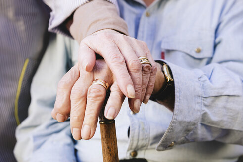 Close-up of old man's and woman's hands resting on a cane - GEMF000147