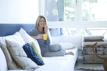 Entspannte Frau auf der Couch sitzend mit einer Tasse Kaffee - MAEF009964