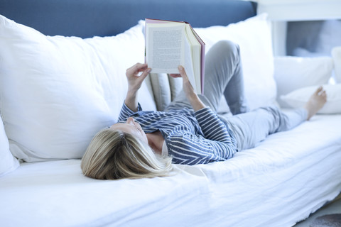 Frau liegt auf der Couch und liest ein Buch, lizenzfreies Stockfoto