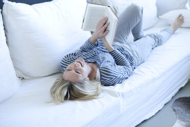 Frau liegt auf der Couch und liest ein Buch - MAEF009982